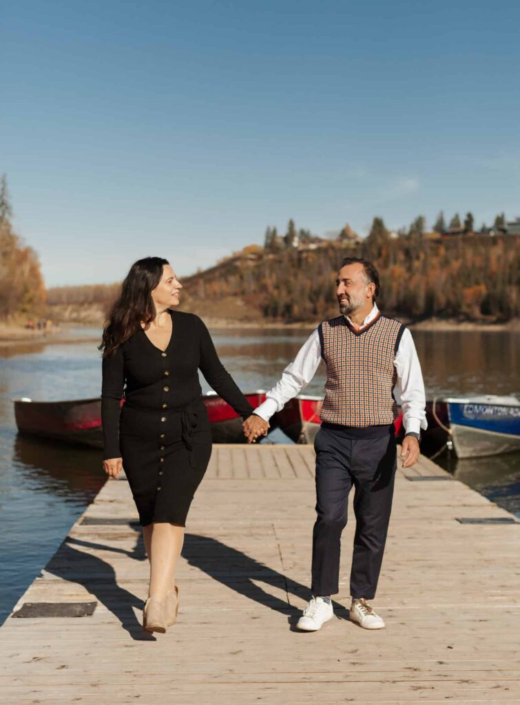 Couple walking on a boardwalk along North Saskatchewan River holding hands and looking at each other