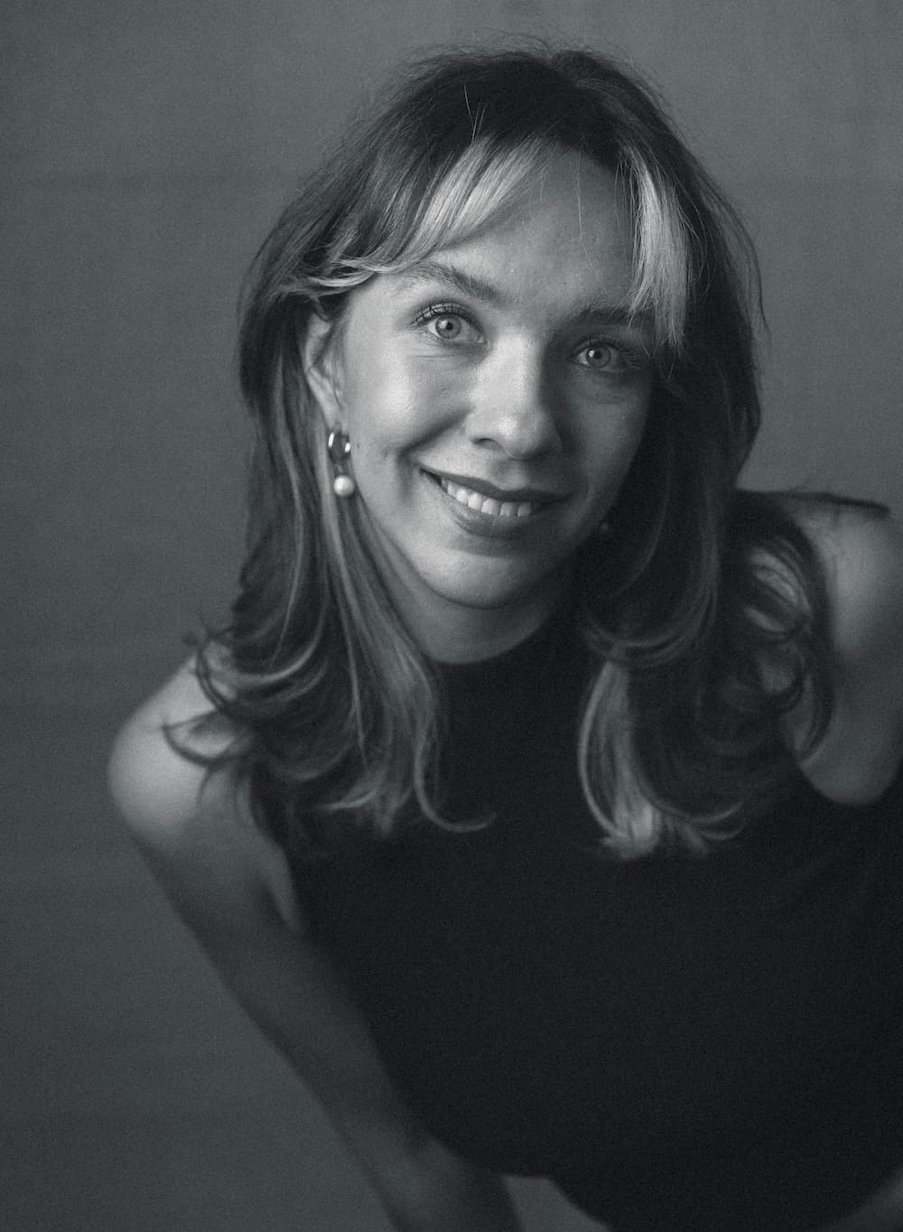 A caucasian woman smiling at the camera with bangs and some blonde highlights