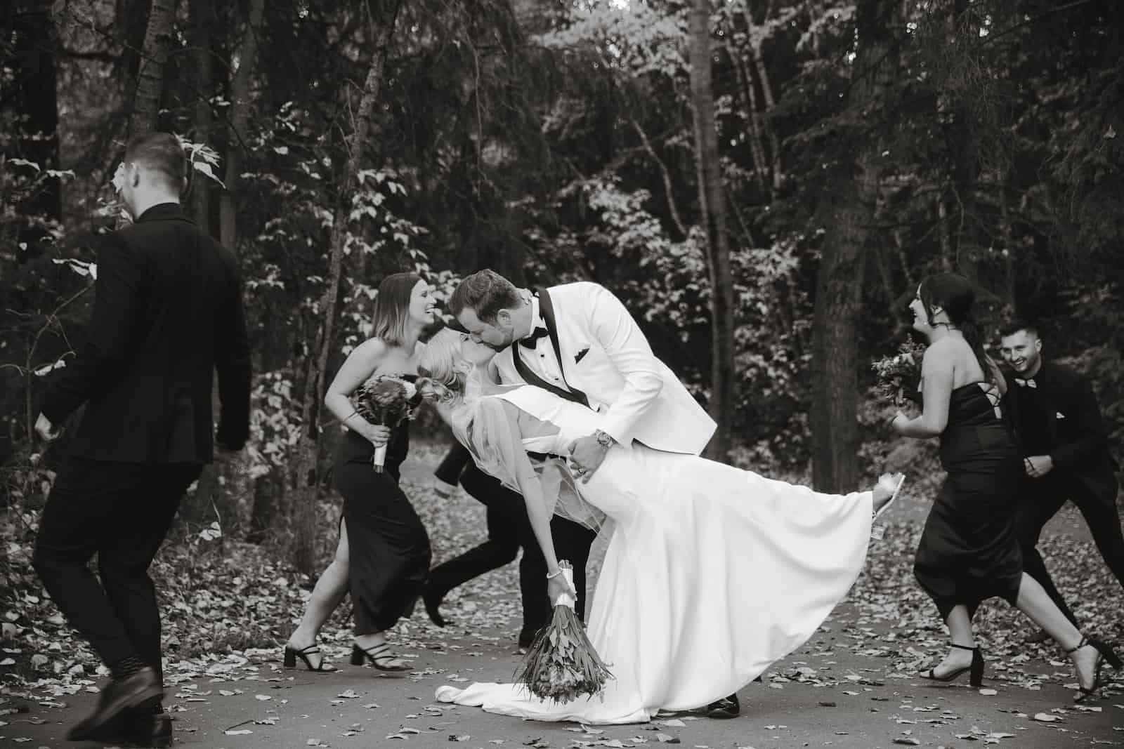 Bride and groom kissing in the woods with their bridal party