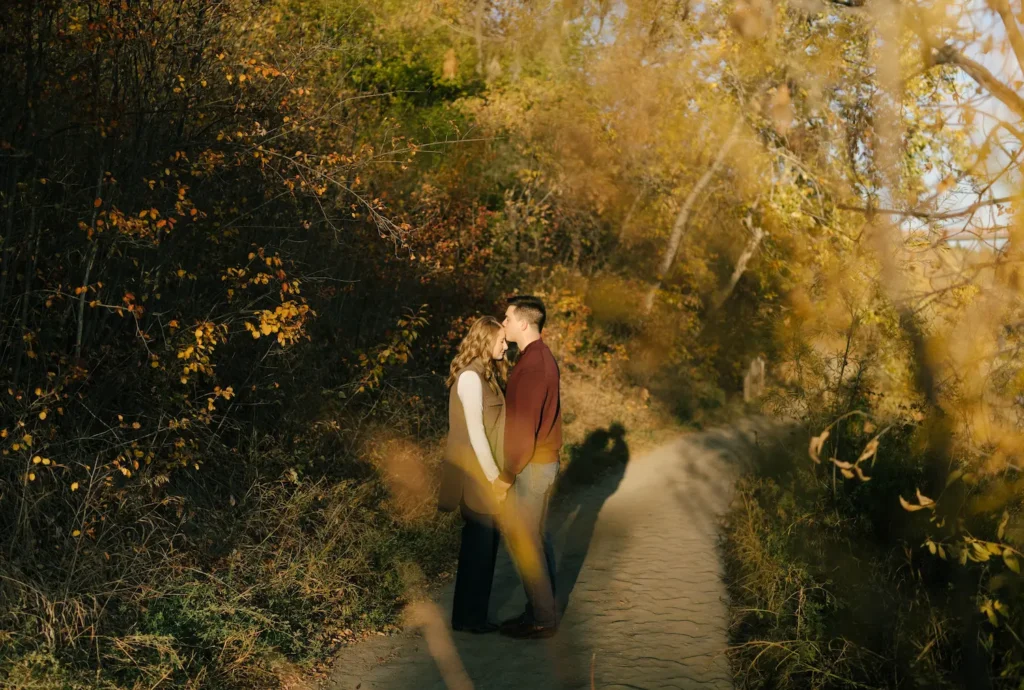 capilano park engagement photos of a couple standing against a fence looking at eachother with a blue sky in the background