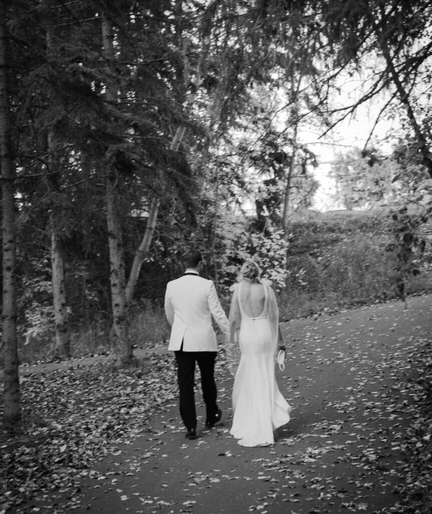 black and white photo of groom and bride holding hands in the edmonton river valley and walking up the path out of the trees