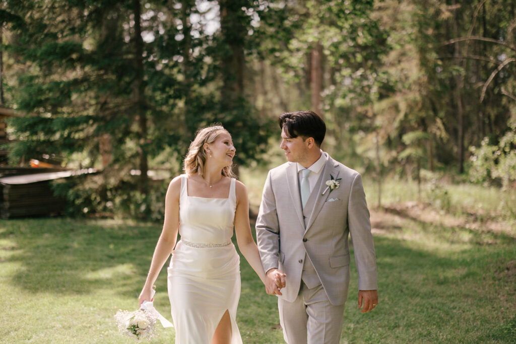 Bride and groom walking hand in hand through a forest after their outdoor wedding near Bonnyville, Alberta