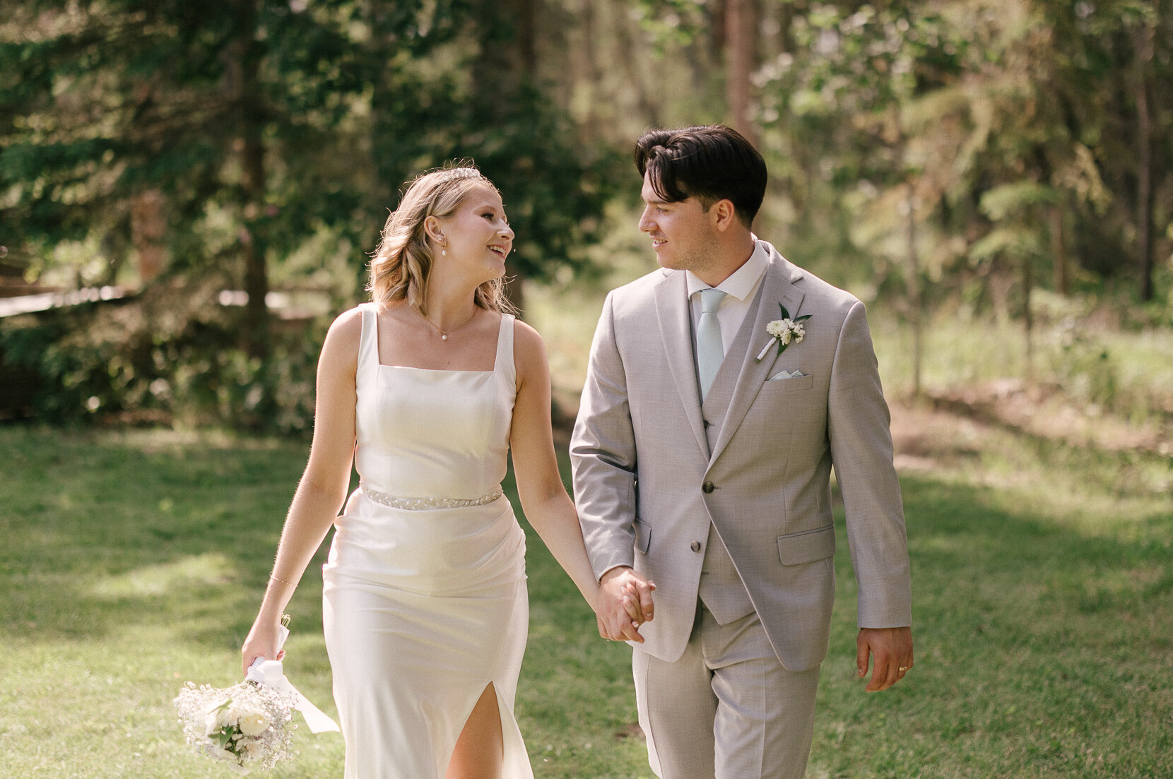 Bride and groom walking hand in hand through a forest after their outdoor wedding near Bonnyville, Alberta