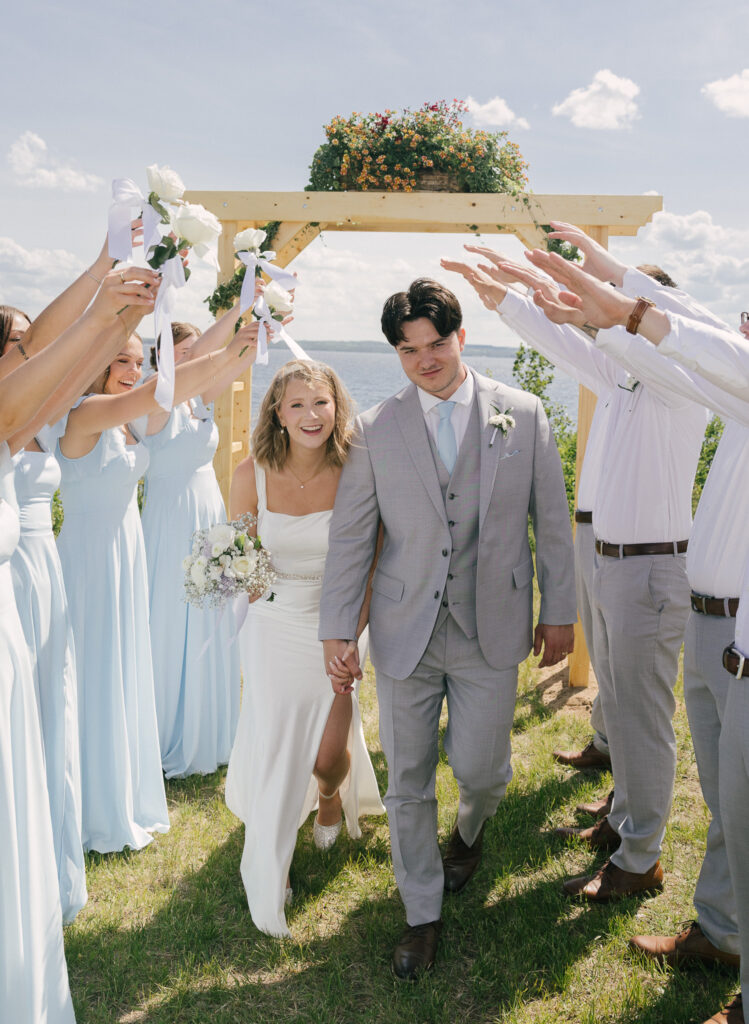 Bride and groom walking through their cheering wedding party after an outdoor lakeside ceremony near Bonnyville, Alberta.