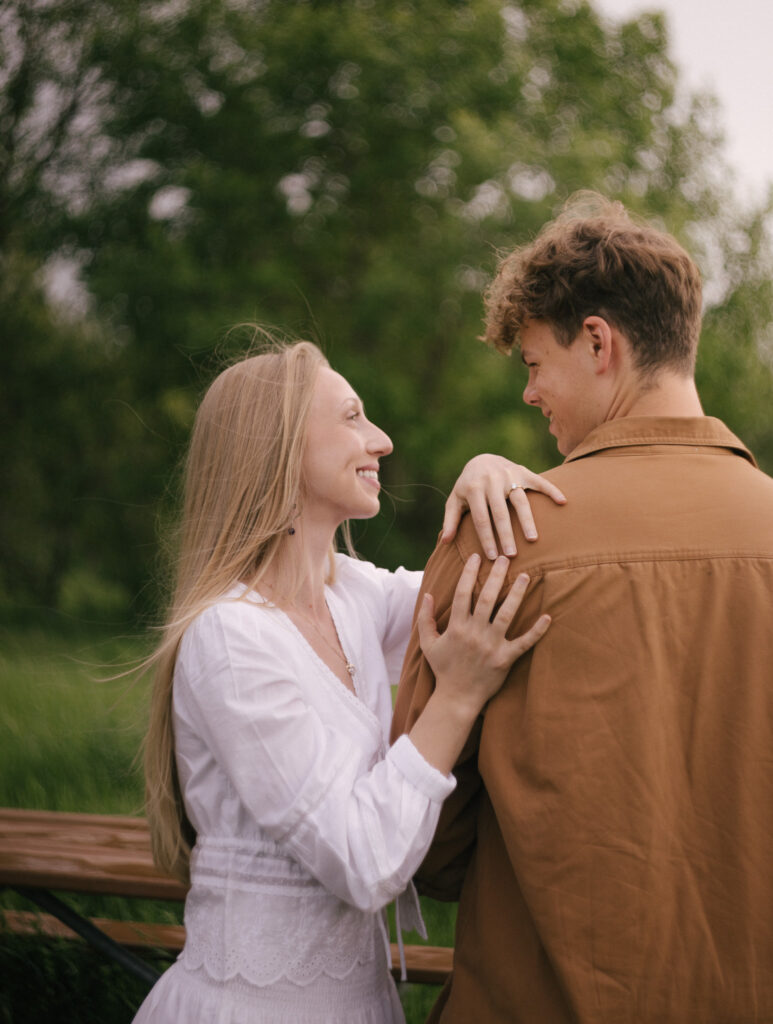 Engaged couple smiling at each other during a summer engagement session at Terwillegar Dog Park in Edmonton, Alberta.