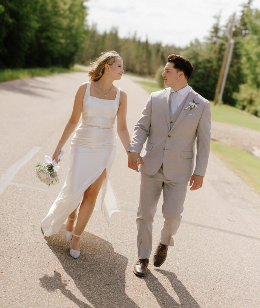 Bride and groom walking together on a rural road in Bonnyville, Alberta